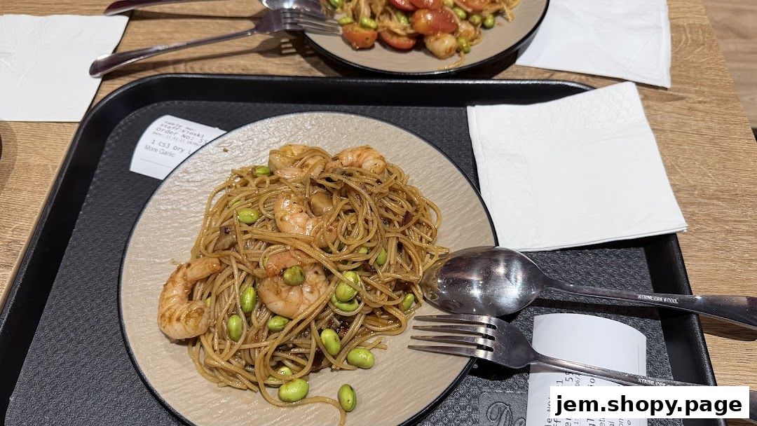 Two plates of pasta with shrimp and edamame beans, served on a tray with napkins.