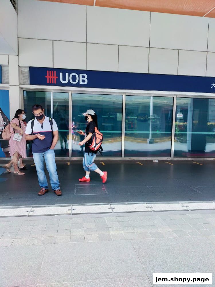 People walk past the UOB bank branch entrance with automatic glass doors.