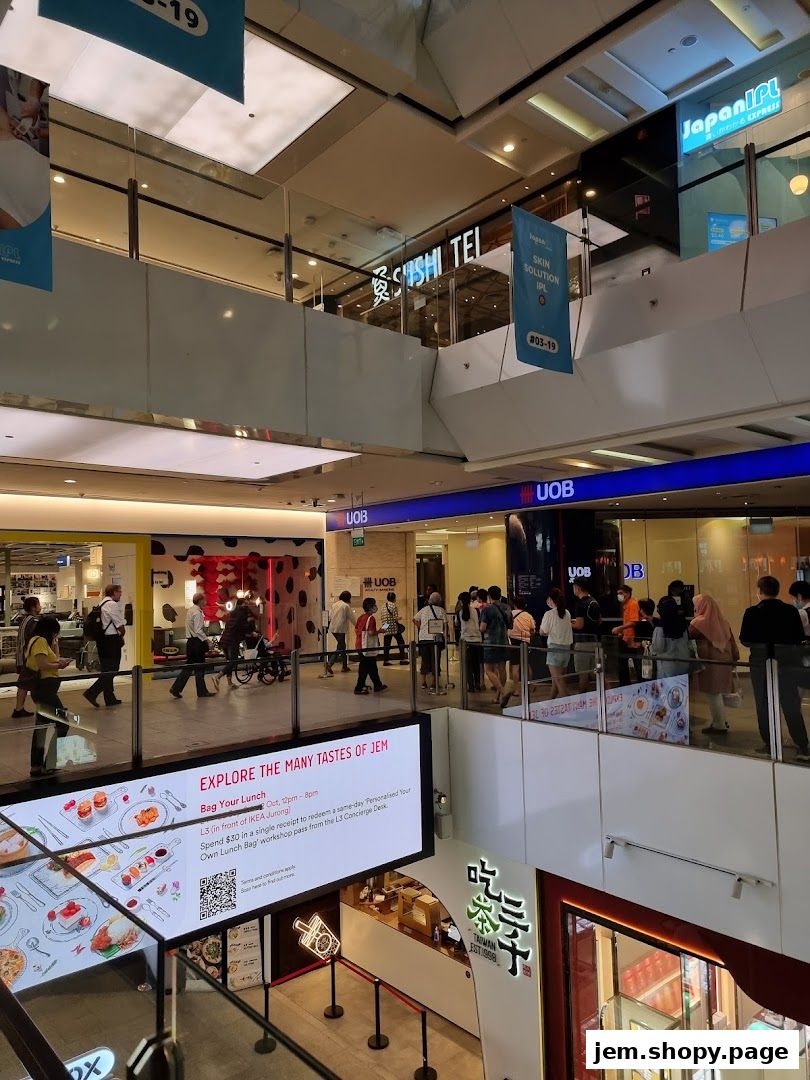 A busy shopping mall interior with various shops and a large digital advertisement.