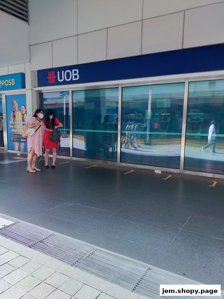 Two women stand outside a UOB bank branch with a POSB advertisement to the left.