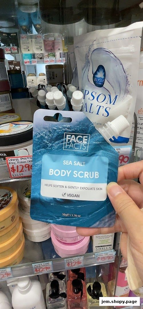 A hand holds a 'Face Facts Sea Salt Body Scrub' product in front of a display of beauty products.