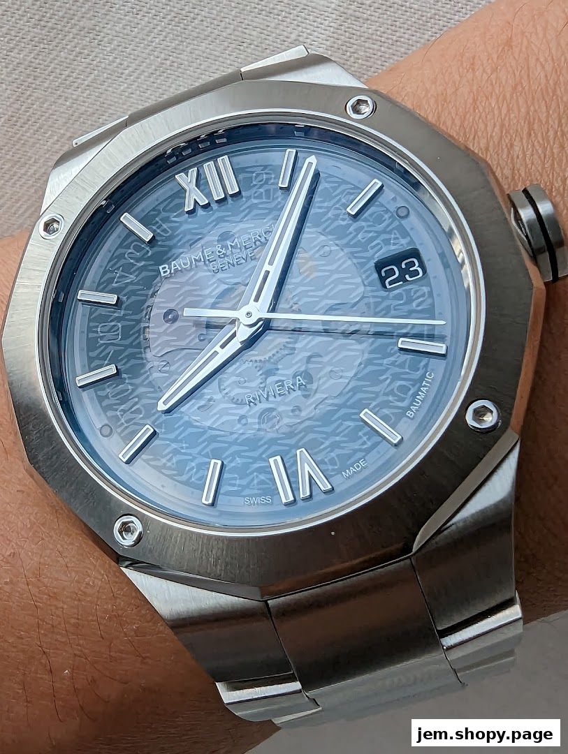 Close-up of a Baume & Mercier Riviera watch with a blue patterned dial on a wrist.