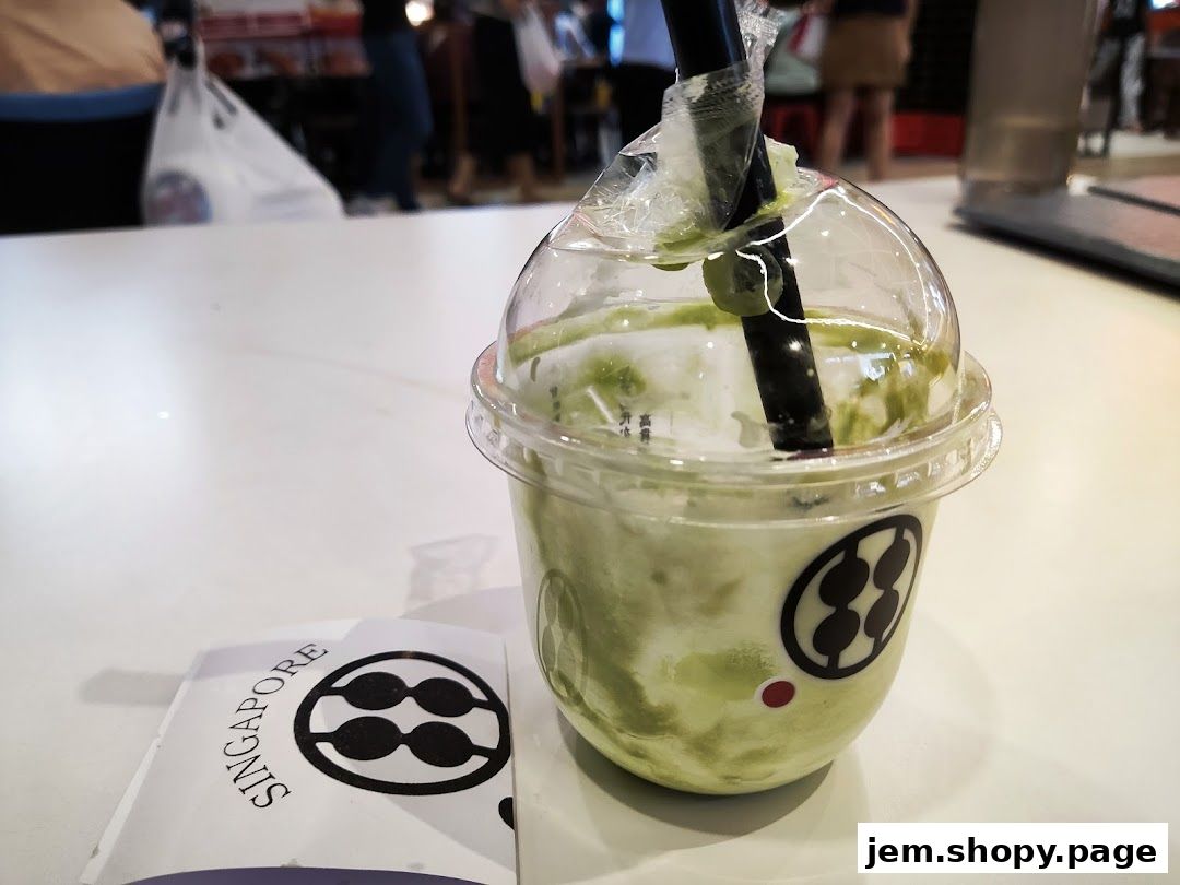 A refreshing green matcha drink with a straw in a clear plastic cup, next to a brochure.