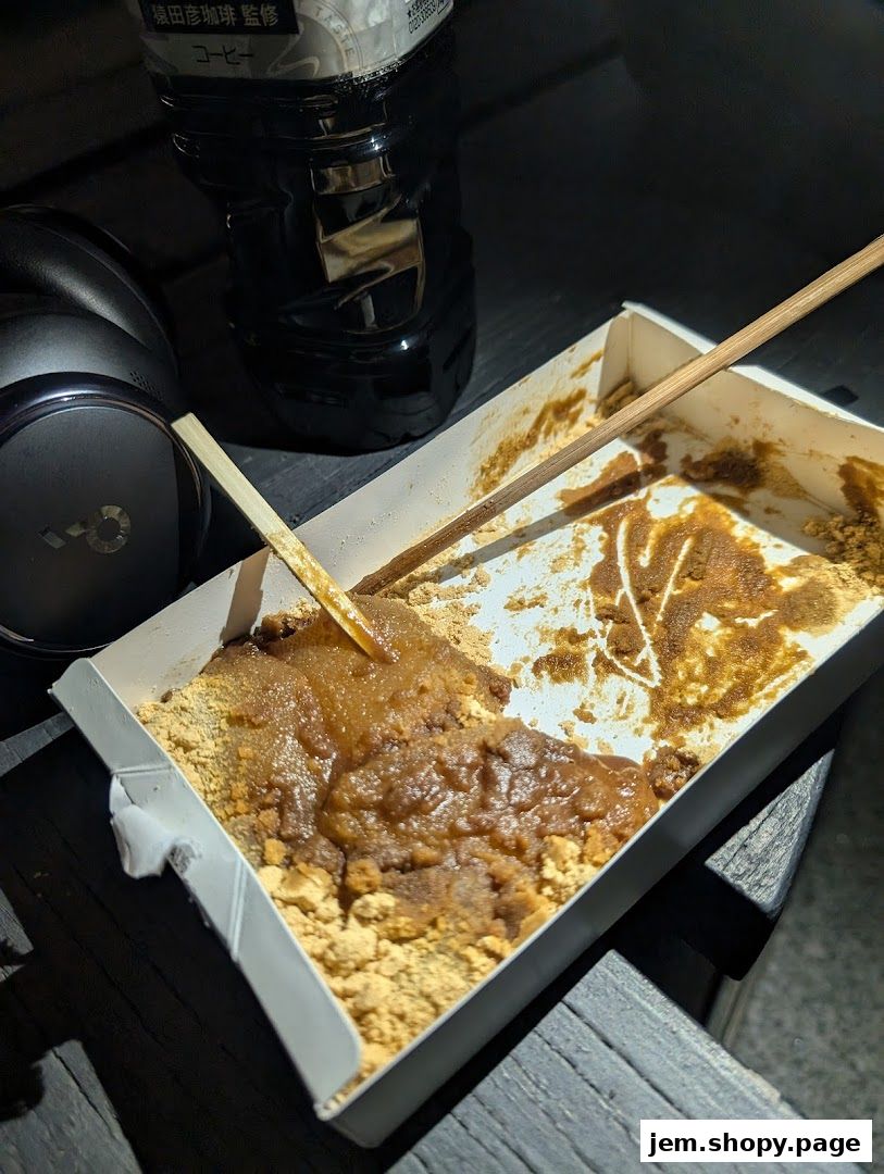 A partially eaten box of warabimochi with chopsticks and a bottle of coffee.