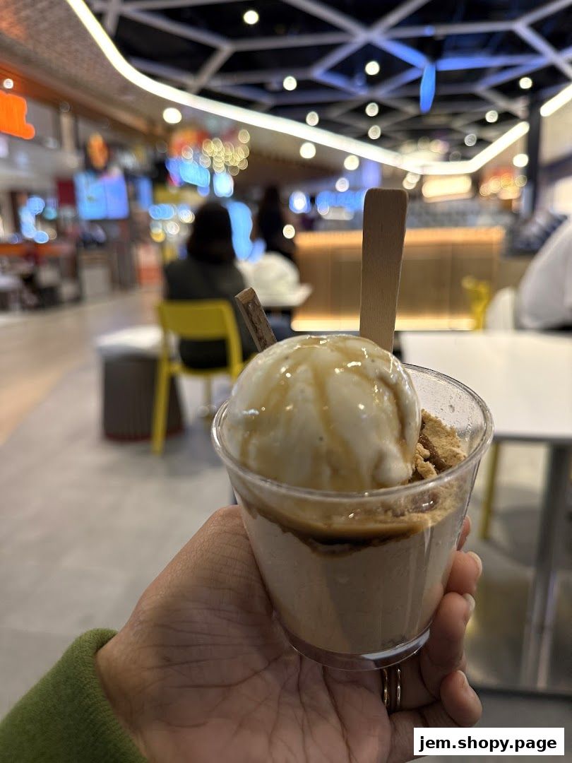 A hand holds a clear cup filled with a layered dessert topped with ice cream.