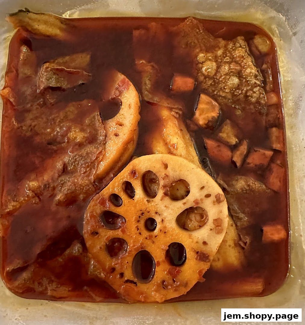A close-up of a dish with fish, lotus root, and vegetables in a rich, red sauce.