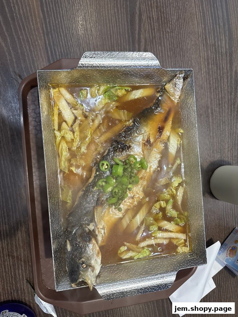 A whole fish dish with vegetables in a metal tray on a wooden table.