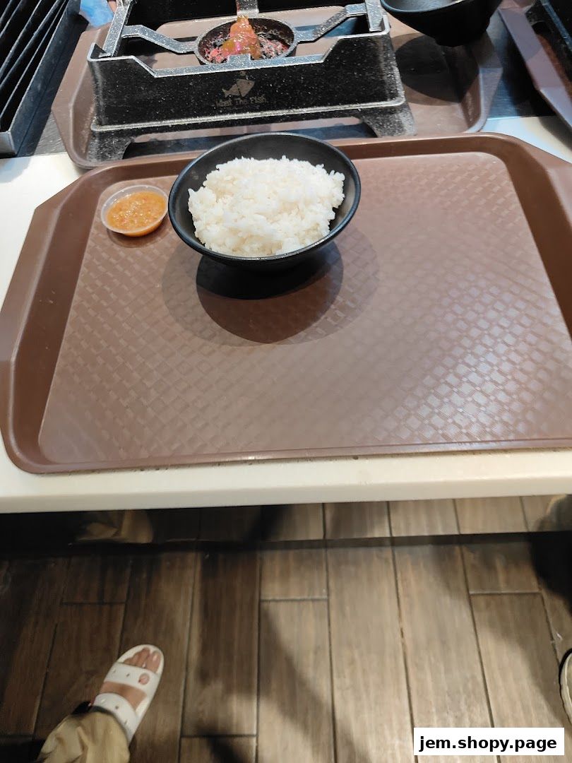 A bowl of white rice and a small dish of sauce on a tray.