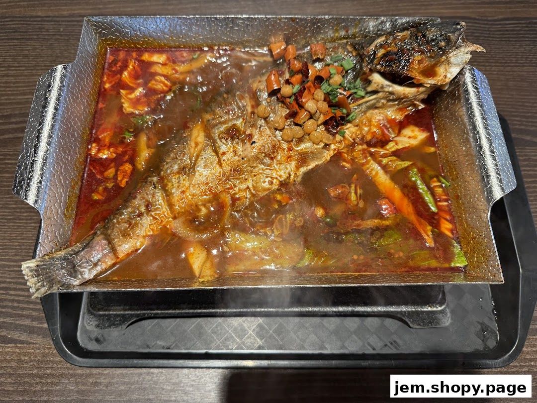 A whole fish dish served in a sizzling platter with spicy broth and vegetables.