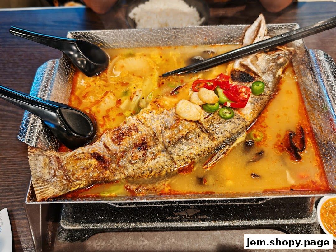 A whole grilled fish in a spicy broth with chili and garlic, served with spoons.