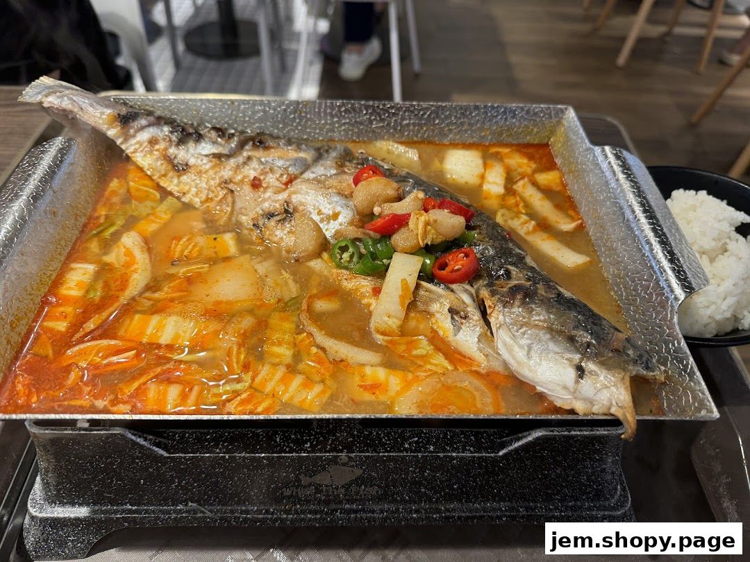 A whole fish dish served in a spicy broth with vegetables and a side of rice.