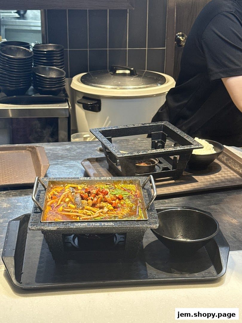 A sizzling dish of fish in spicy broth is presented on a portable burner at What The Fish.