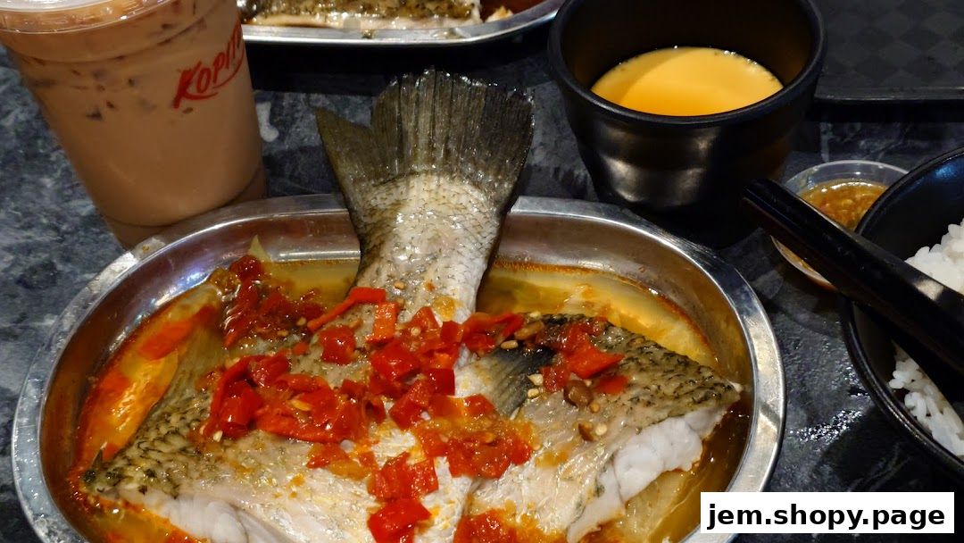 A whole steamed fish dish with chili, served with rice and a drink.
