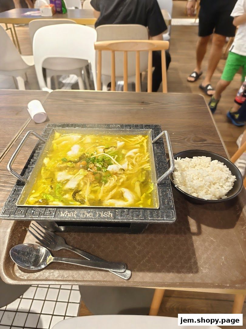 A steaming bowl of fish soup with rice and cutlery on a table.