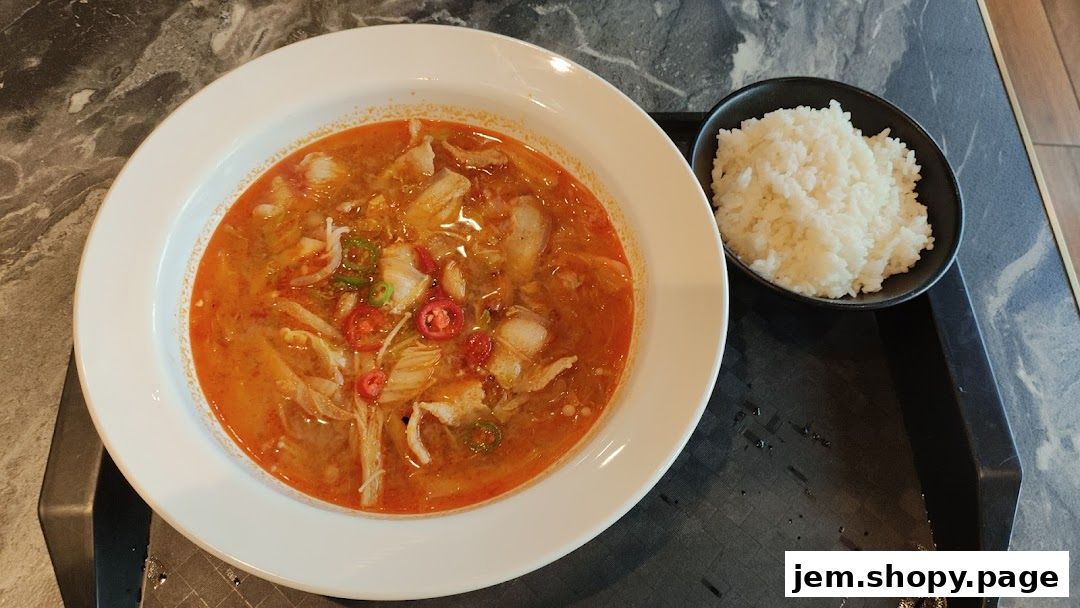 A bowl of spicy fish soup with rice, garnished with chili slices and green onions.