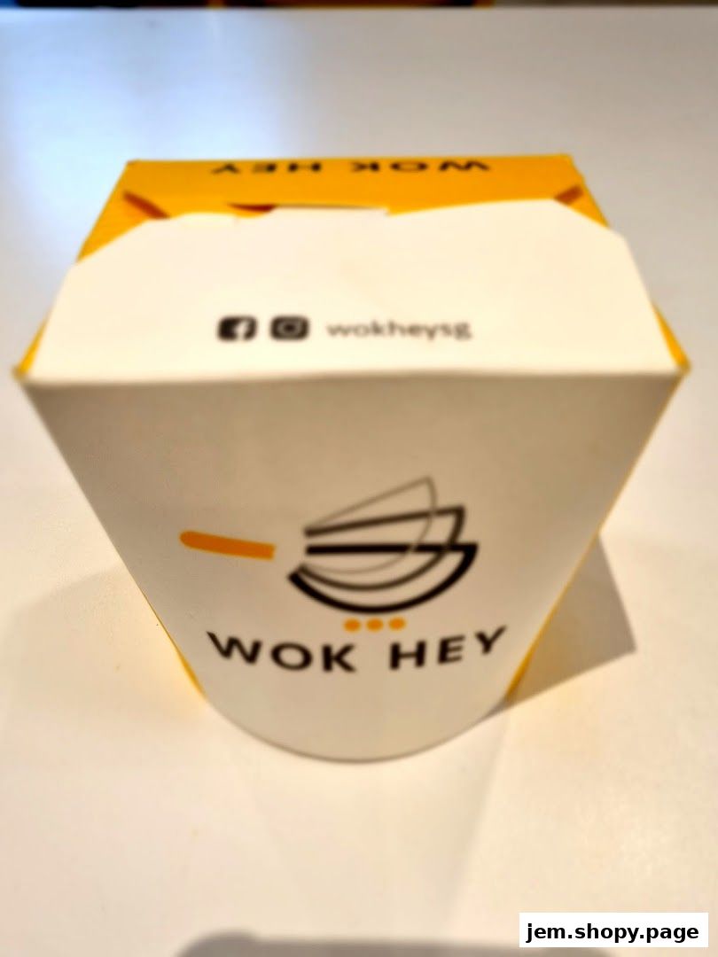 A white takeout box with the WOK HEY logo and social media handles.