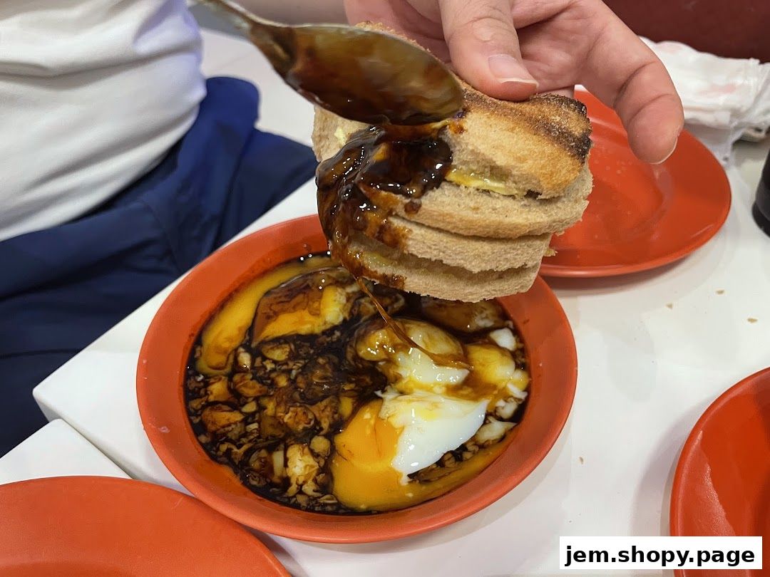 A hand dips toast into a bowl of soft-boiled eggs and soy sauce.