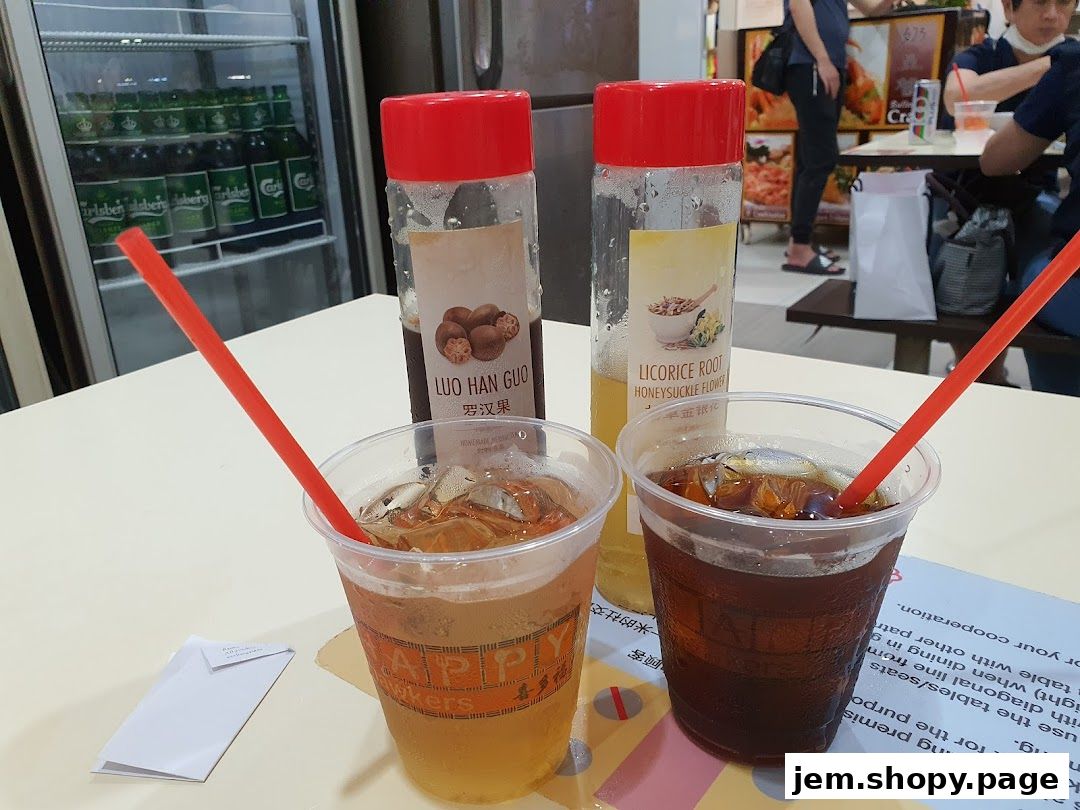 Two iced drinks and two bottles of flavored syrup on a table at Ya Kun Kaya Toast.