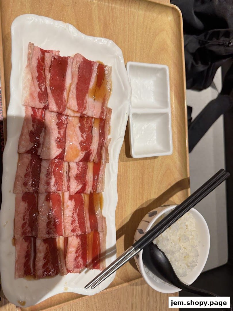 A plate of thinly sliced raw beef, rice, and chopsticks on a wooden tray.