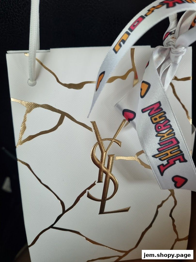 A white Yves Saint Laurent shopping bag with gold accents and a decorative ribbon.