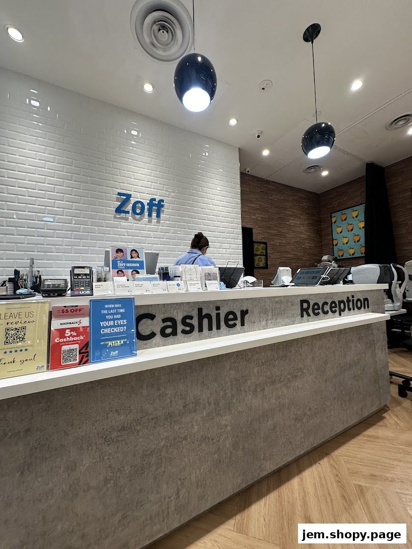 The reception and cashier counter of a Zoff optical shop with a tiled wall and modern lighting.