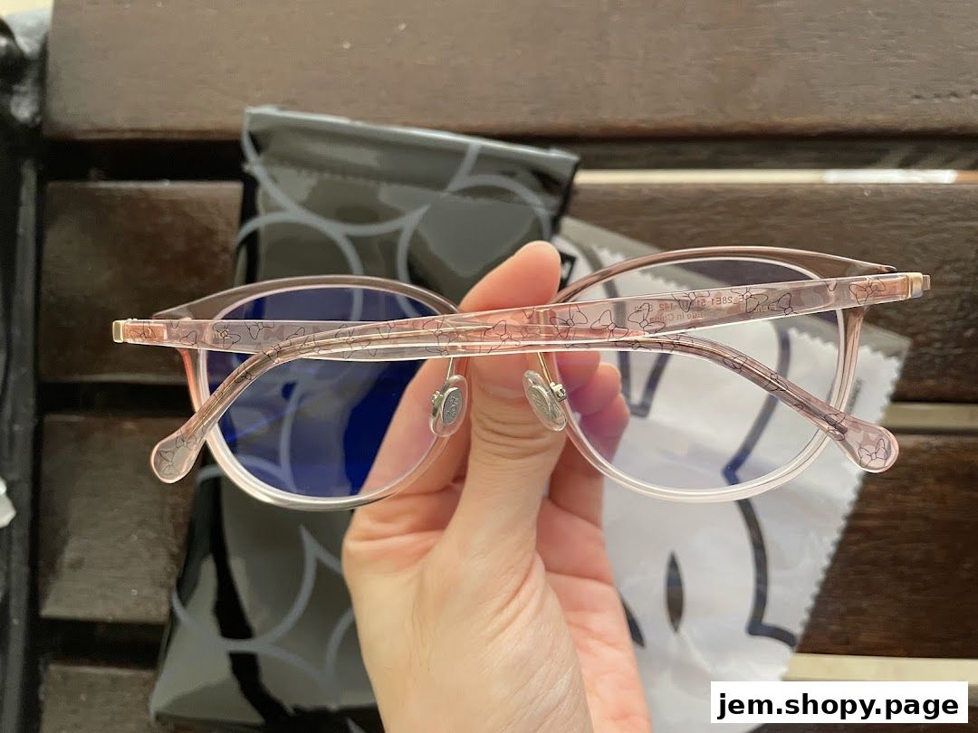 A hand holds up a pair of pink glasses with a subtle bow pattern.