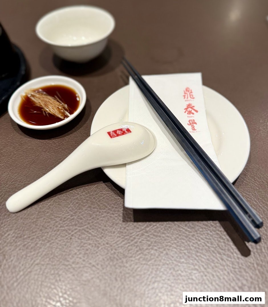A table setting at Din Tai Fung with chopsticks, a spoon, a bowl of soy sauce, and a plate.