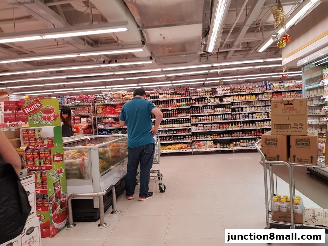 A man shops in a well-stocked supermarket aisle with shelves full of various products.