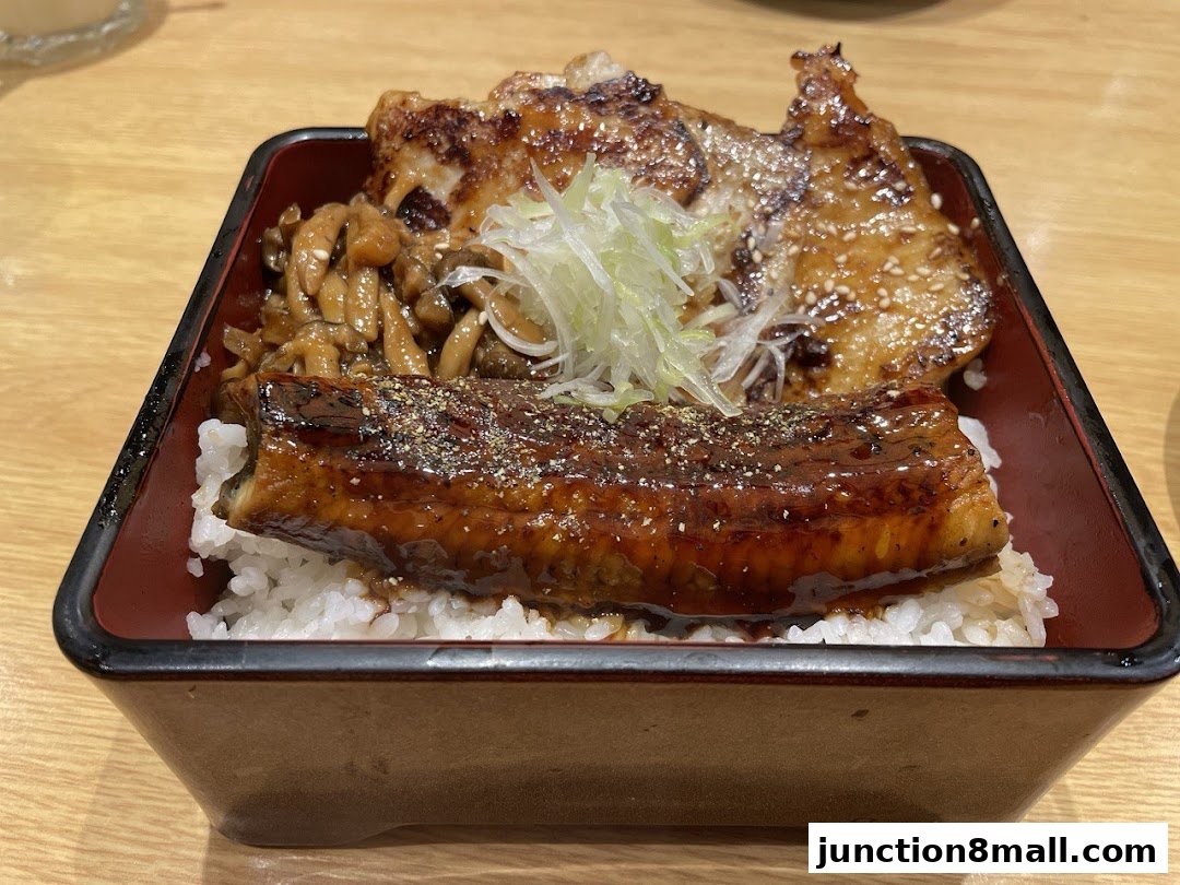 A close-up of a Japanese rice bowl dish with grilled eel, chicken, and mushrooms.