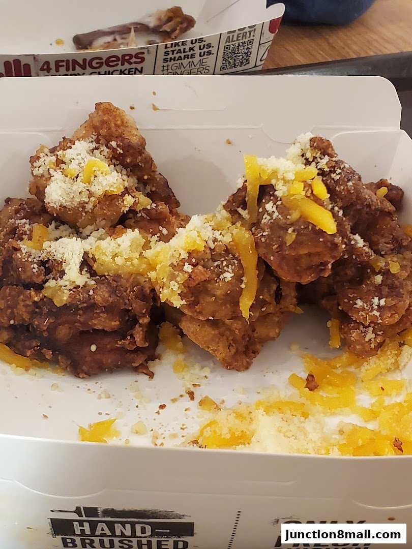 Crispy fried chicken pieces topped with shredded cheese in a takeaway box.