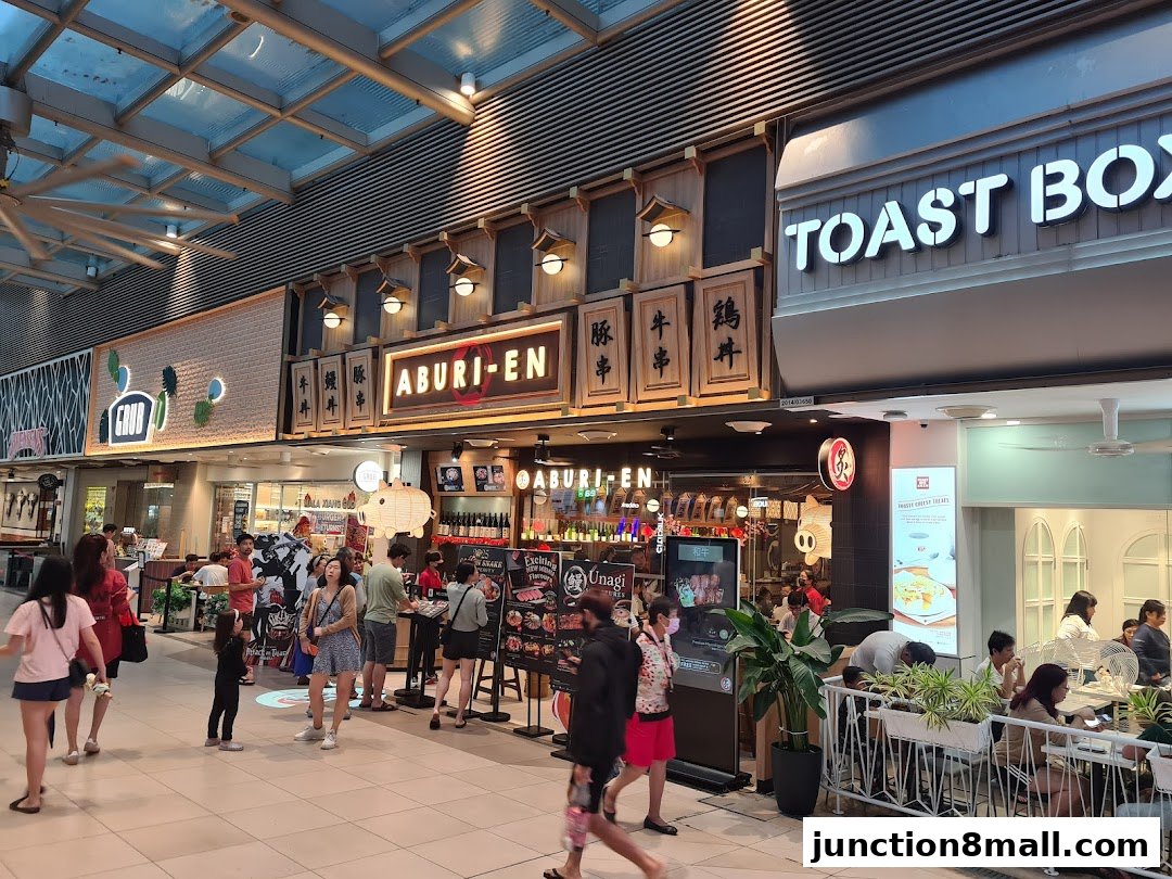 A busy shopping mall walkway with several food establishments, including Aburi-EN and Toast Box.