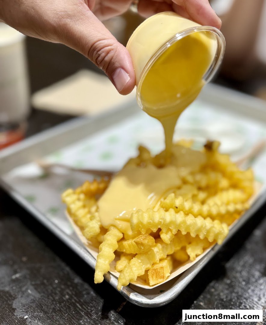 A hand pours cheese sauce over a serving of crinkle-cut fries.