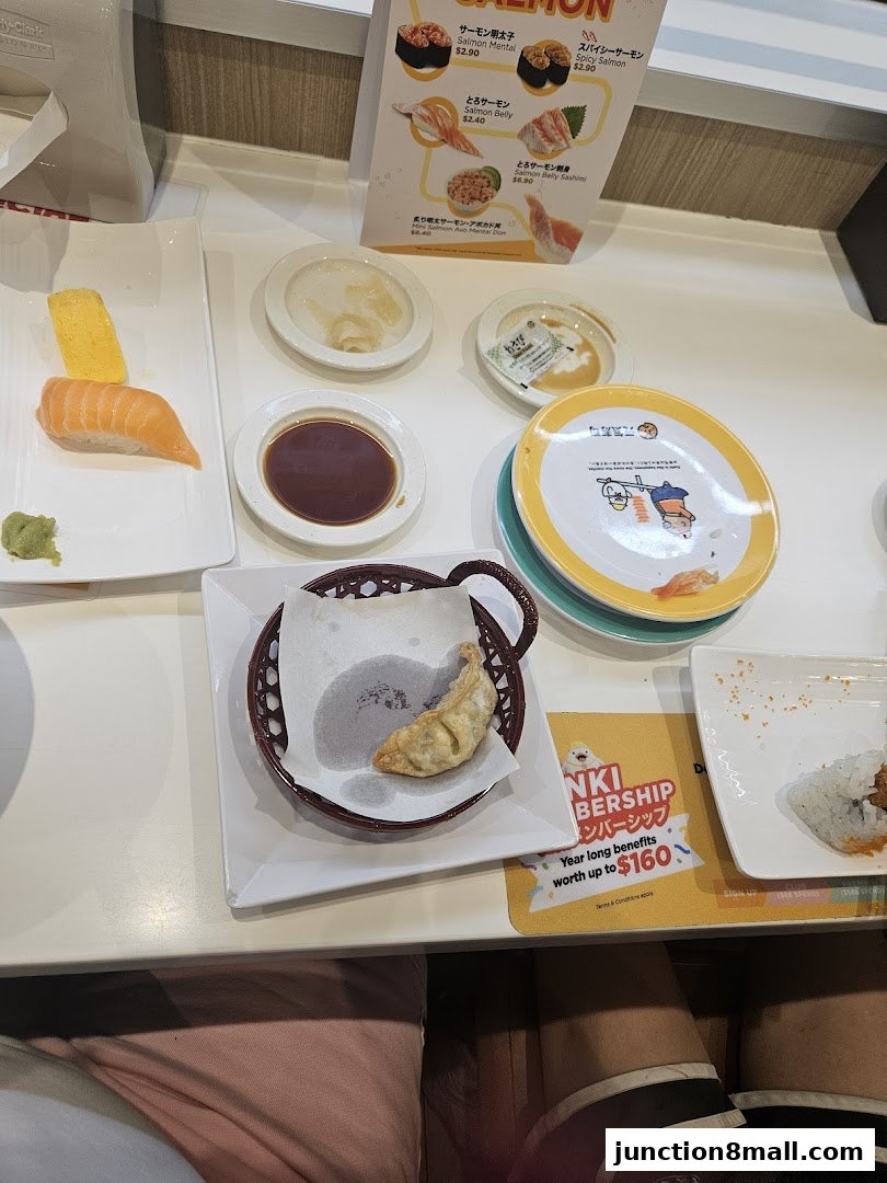 A table at Genki Sushi Junction 8 with various sushi dishes, dipping sauce, and a fried dumpling.