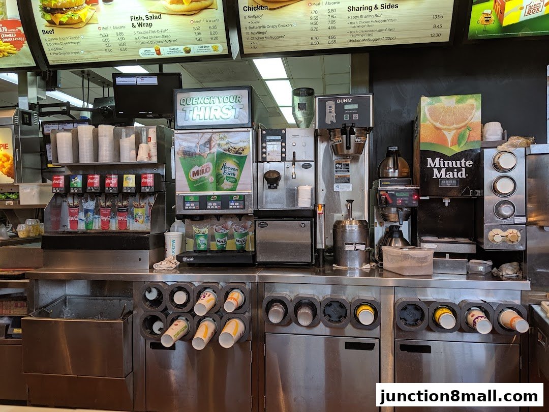 A McDonald's beverage station with drink dispensers, cups, and menu boards.