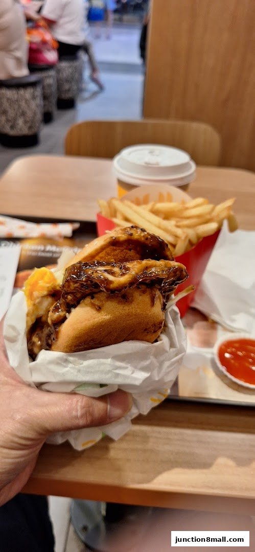 A hand holds a burger with fries and a drink at McDonald's.
