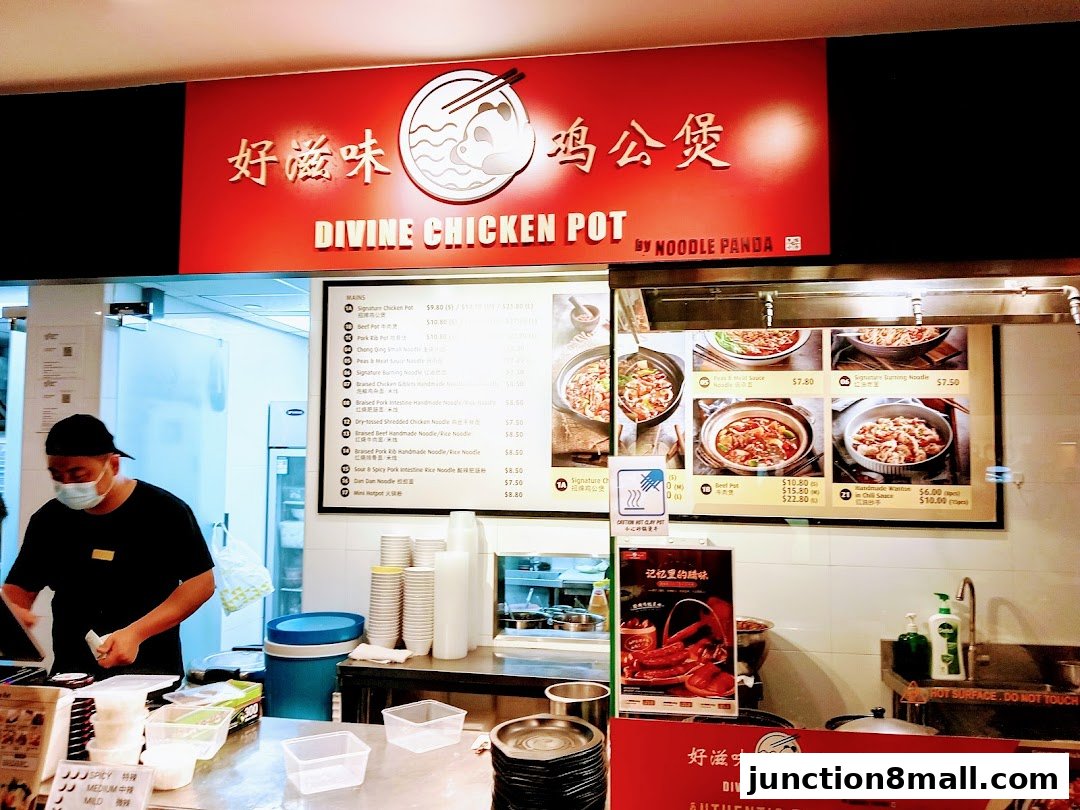 A food stall counter with a menu board displaying various chicken pot dishes and a staff member preparing food.