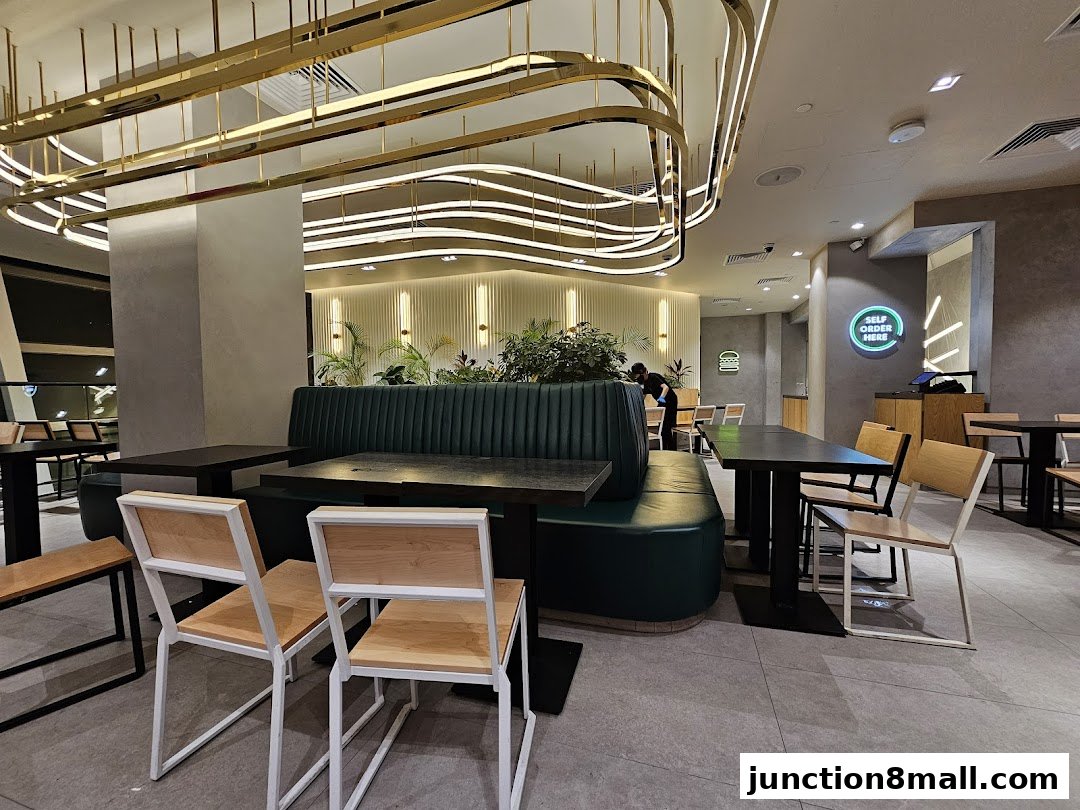 Interior of a modern restaurant with green booths, tables, chairs, and decorative lighting.