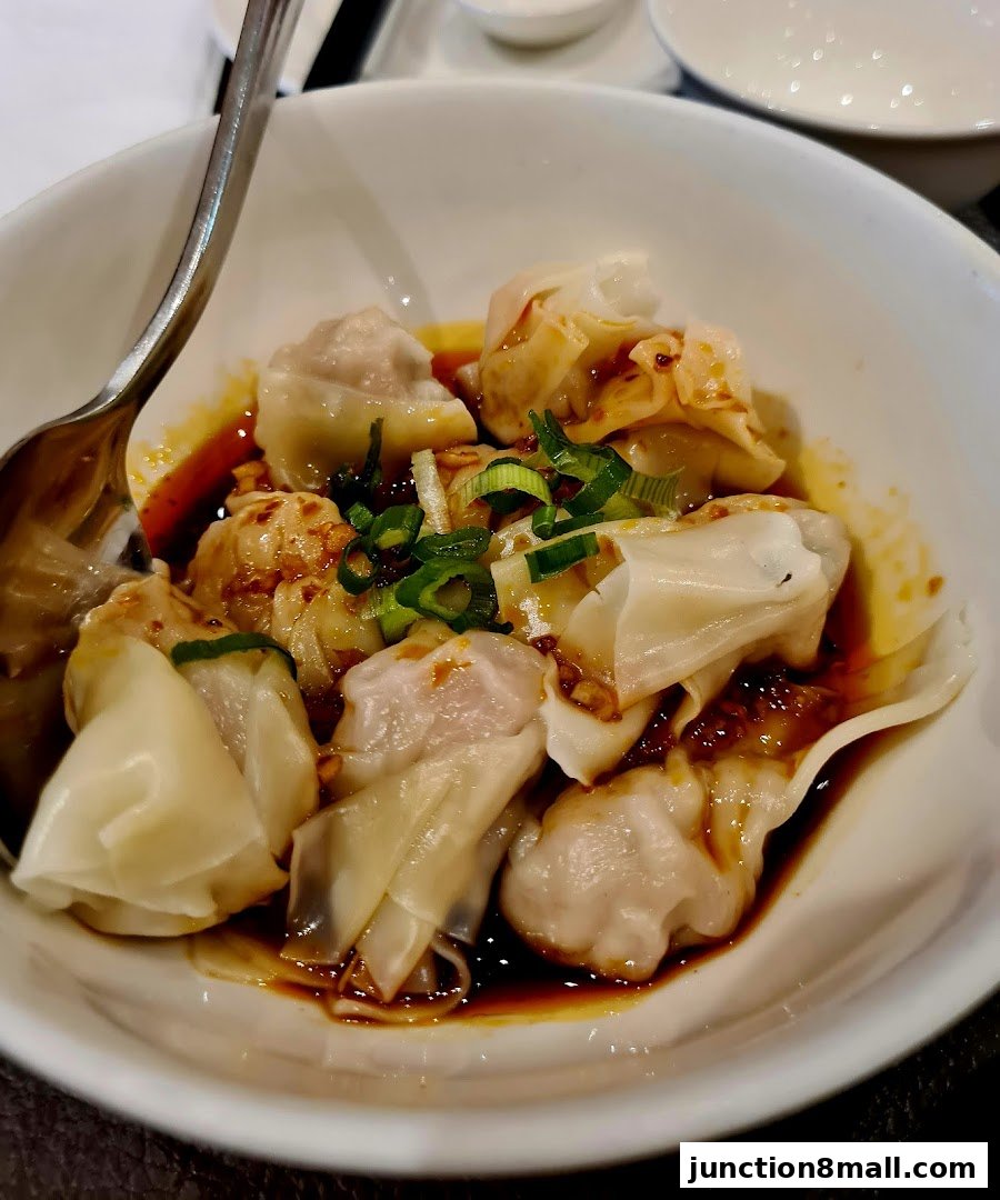 A bowl of delicious wontons in chili oil, garnished with chopped scallions.