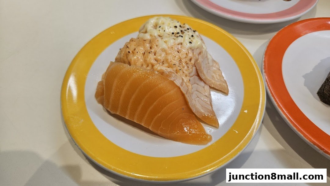 A plate of salmon sushi with creamy topping and another plate with a piece of sushi.