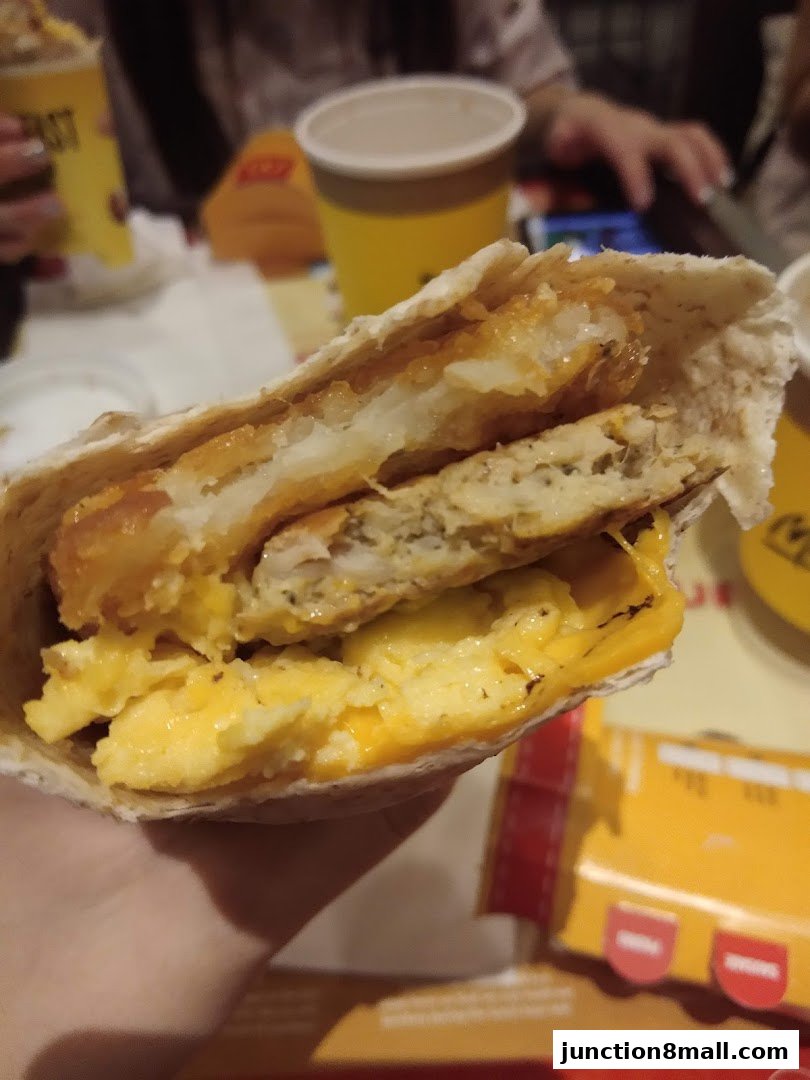 A close-up of a breakfast wrap filled with scrambled eggs, cheese, and a hash brown.