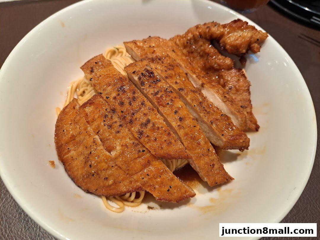 A close-up shot of sliced pork chop served over noodles in a white bowl.