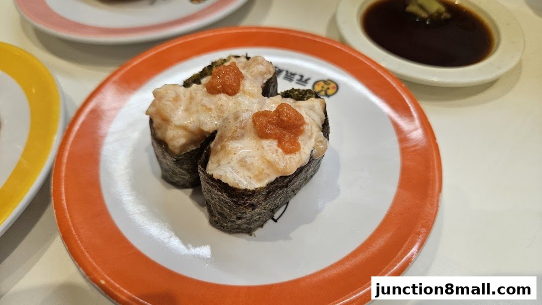 Close-up of two pieces of sushi with creamy topping and roe on a white plate with orange trim.