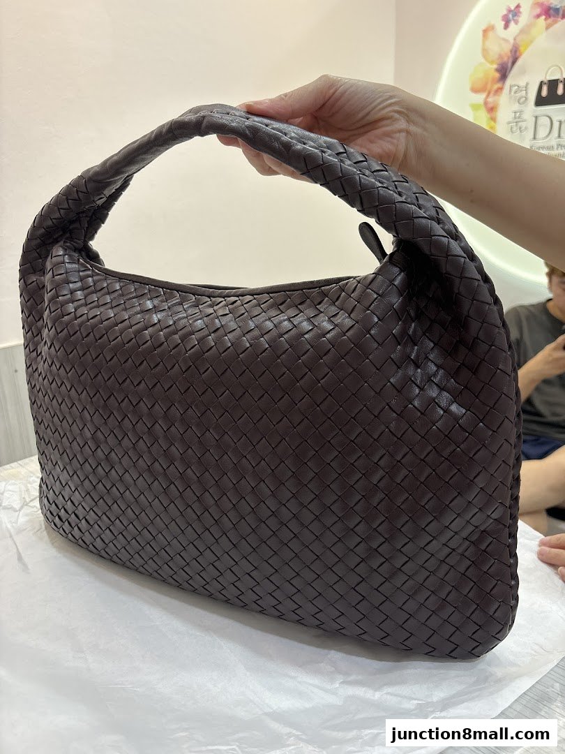 A person holds a dark brown woven leather handbag.