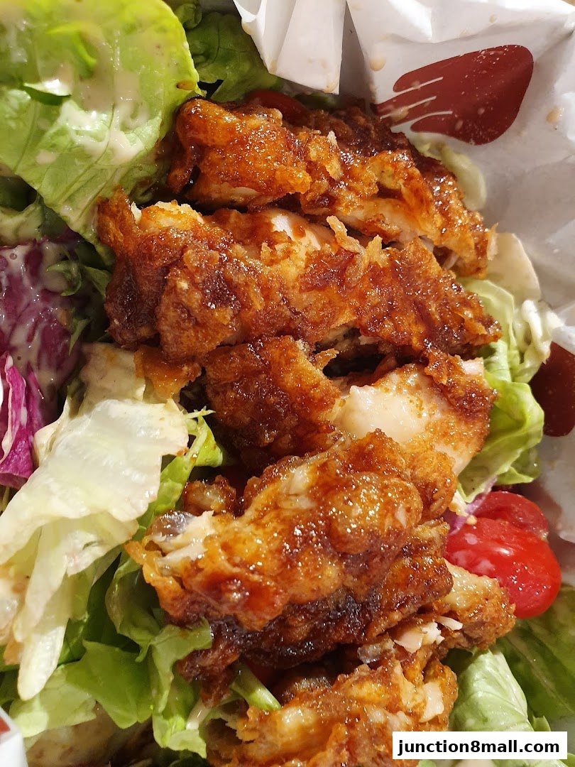 A close-up shot of crispy fried chicken pieces served over a fresh salad with dressing.