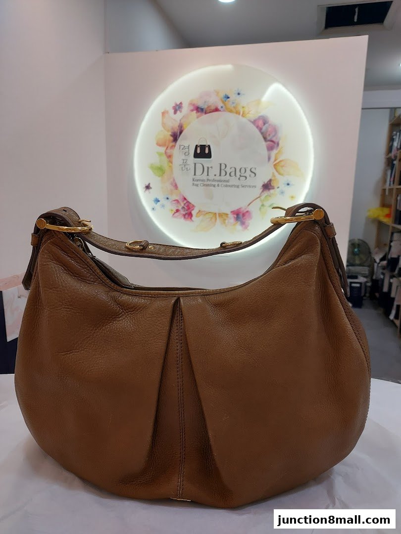 A brown leather handbag is displayed in front of a circular logo for Dr. Bags.