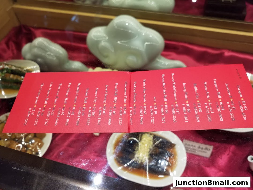 A red card listing various Din Tai Fung locations and contact numbers, displayed in a shop window.