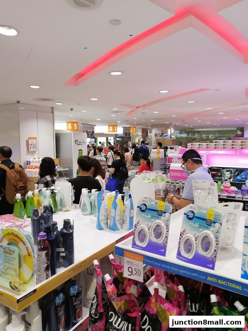 A busy FairPrice Finest supermarket aisle with shoppers and various household products on display.