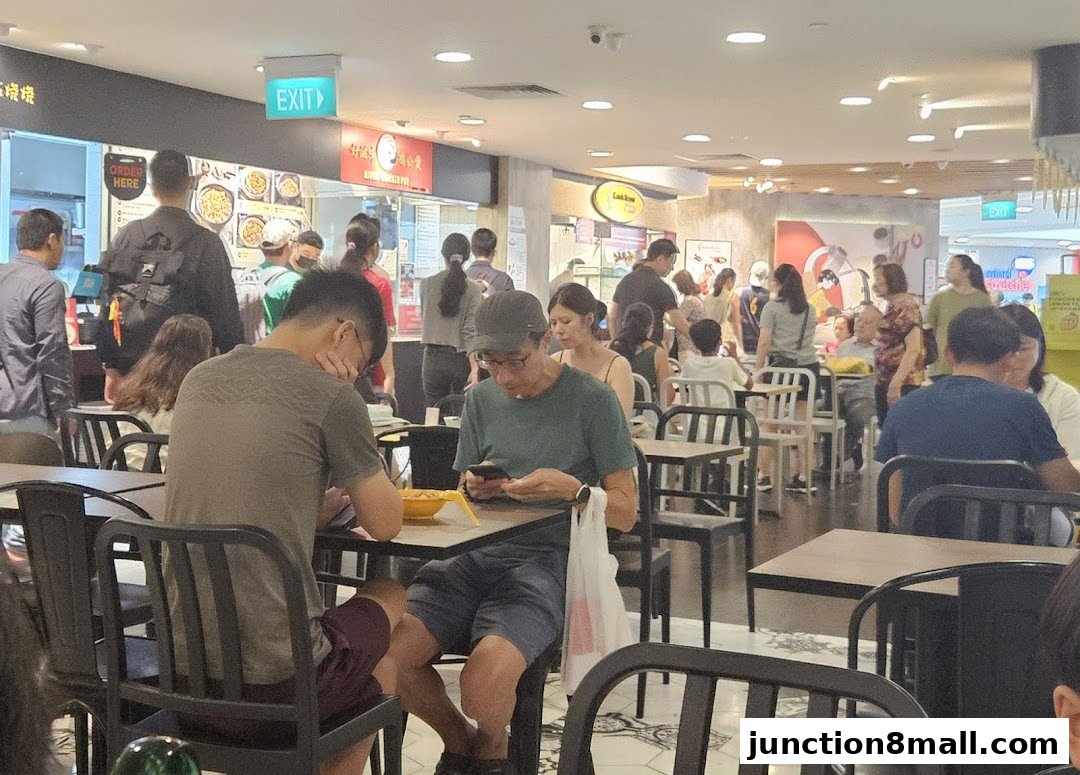 People dining and queuing at a busy food court with various food stalls visible.