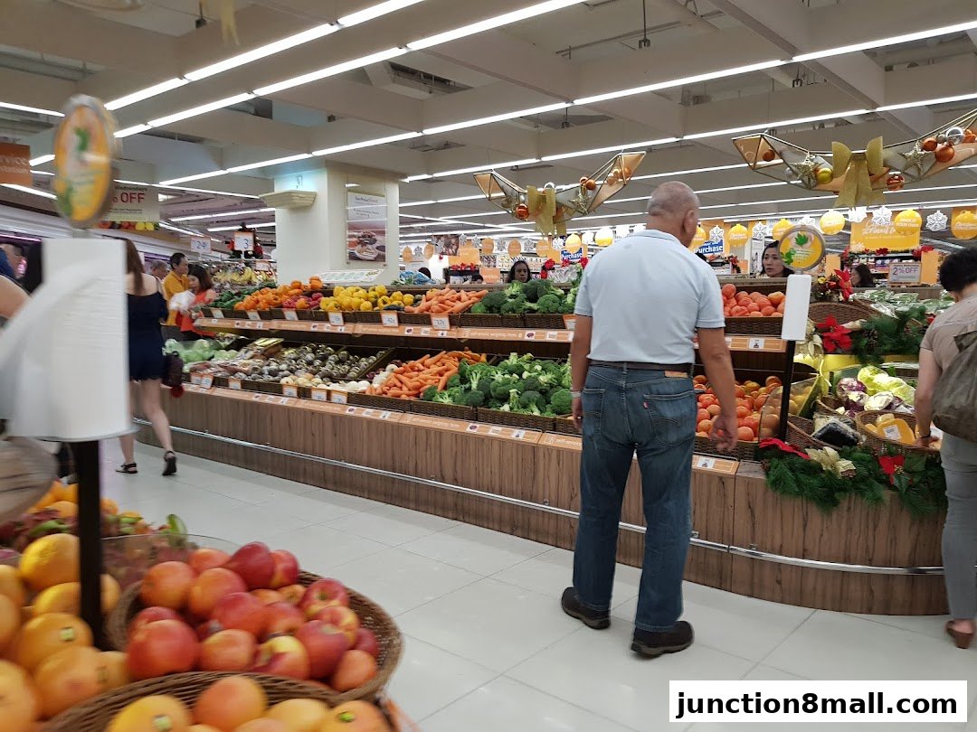Customers browse fresh produce displays in a well-lit supermarket aisle.