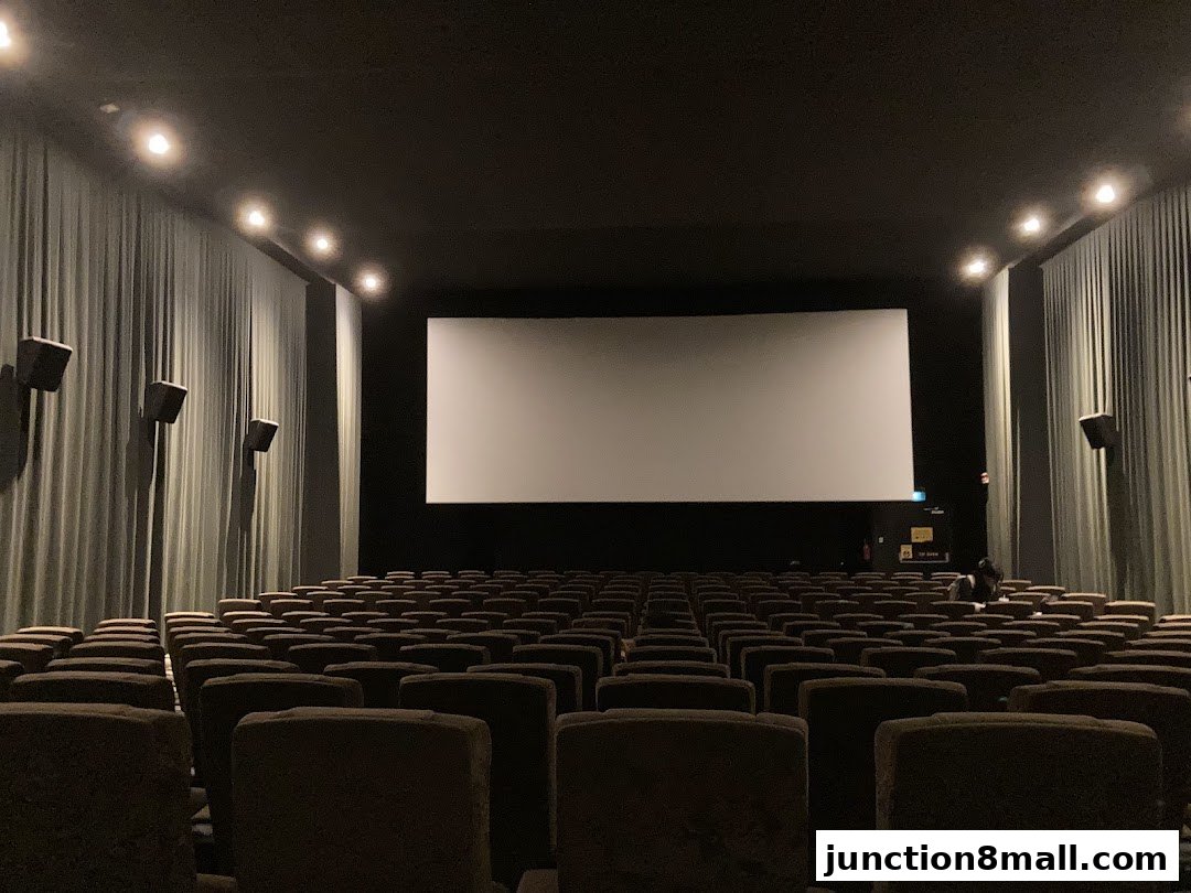 An empty cinema hall with rows of seats facing a large blank screen.
